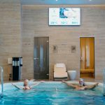 Two adults enjoying leisure time at an indoor swimming pool with spa-like ambiance.