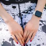 A smartwatch worn on a person's wrist with athletic leggings in an outdoor setting.
