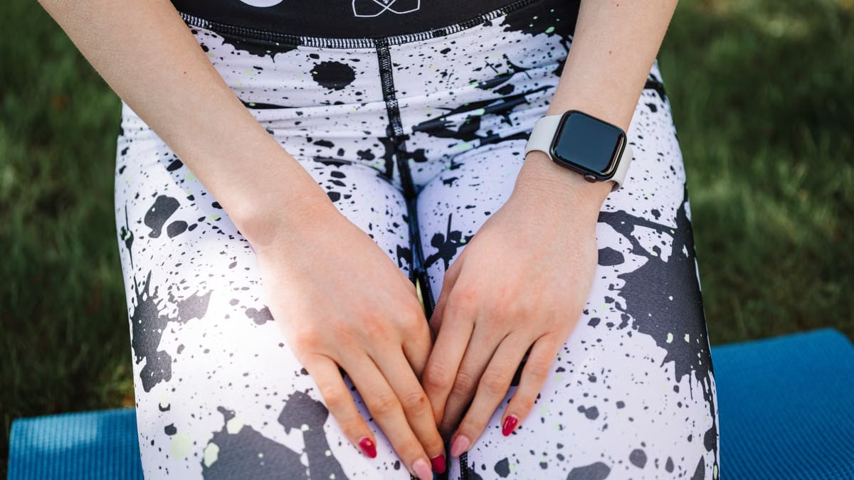 A smartwatch worn on a person's wrist with athletic leggings in an outdoor setting.